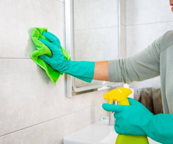 Close up of woman's hands cleaning bathroom tiles with a microfiber cloth and spray cleaner. High resolution 42Mp indoors digital capture taken with SONY A7rII and Zeiss Batis 40mm F2.0 CF lens