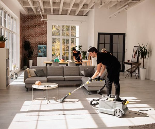 Group of experienced cleaners collaborating to deep clean a spacious apartment. Male worker is vacuuming the carpet.